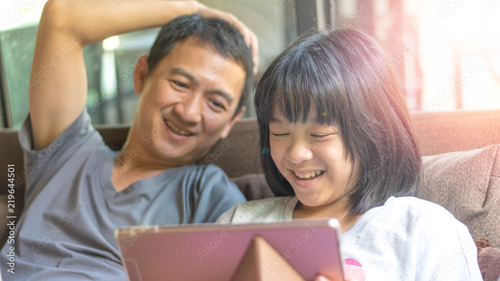 Father and daughter activity technology together concept. Asia kid girl reading e-book or playing game on computer tablet while dad watching as parental guidance for PG13. Father and daughter activity technology together concept. Asia kid girl reading e-book or playing game on computer tablet while dad watching as parental guidance for PG13.
