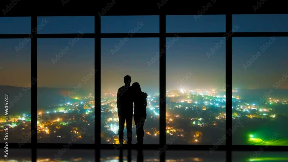 The couple standing near windows on the night city background. time lapse The couple standing near windows on the night city background. time lapse