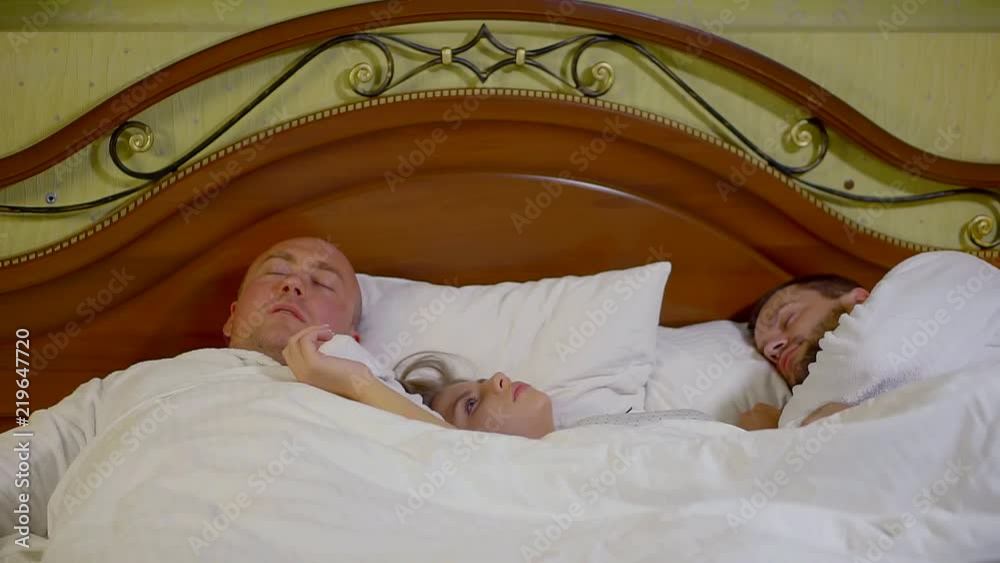 young pretty woman is waking up in bed with two unknowns men in morning in hotel room young pretty woman is waking up in bed with two unknowns men in morning in hotel room