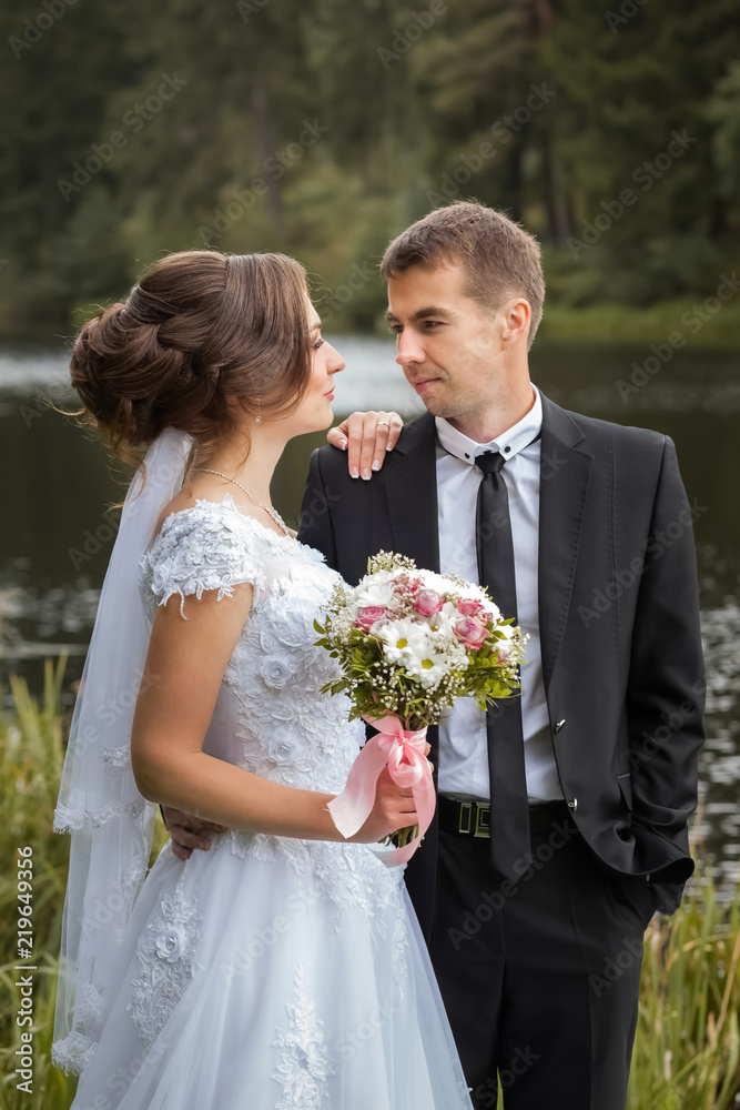 Happy wedding couple. Bride and groom are embracing in the park against the background of the pond. Sunny autumn day Happy wedding couple. Bride and groom are embracing in the park against the background of the pond. Sunny autumn day