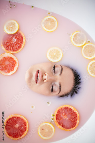 Woman glamour face only, beauty spa and wellness treatment with colorful citrus slices bath with milk moisturizing effect. Healthy Skin, Enjoyment, Pleasure, Therapy, Rejuvenation concept. photo