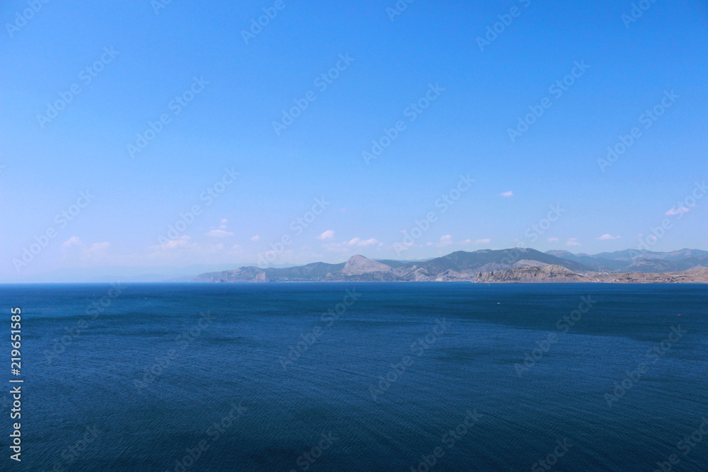 Panoramic view of Black sea with blue air. Black Sea, Crimea. Mountain relief disappearing on the horizon in a foggy haze on a hot summer day. Panoramic view of Black sea with blue air. Black Sea, Crimea. Mountain relief disappearing on the horizon in a foggy haze on a hot summer day.
