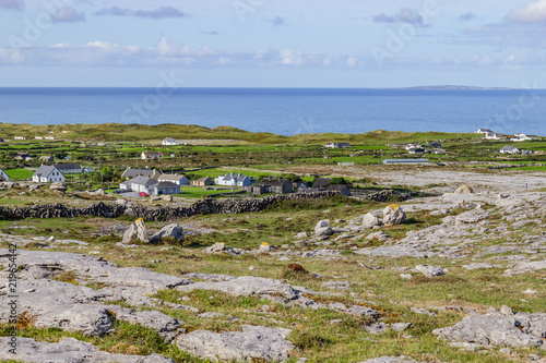 Farms and rocks in hiking trail in Burren way with Aran Islands in background photo