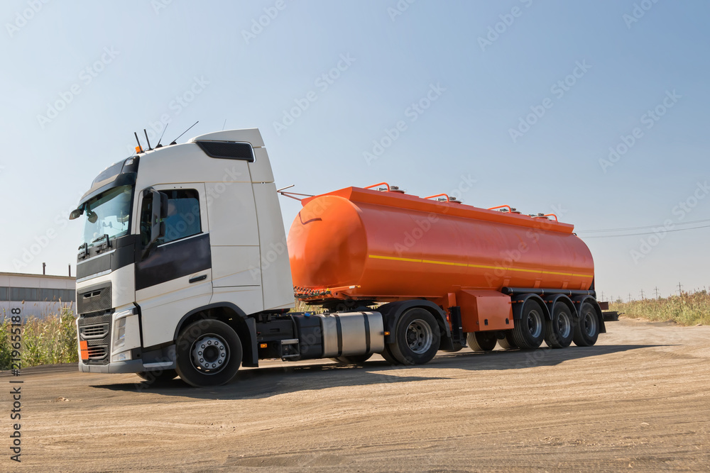 A truck with an orange tank goes on a knurled unpaved road