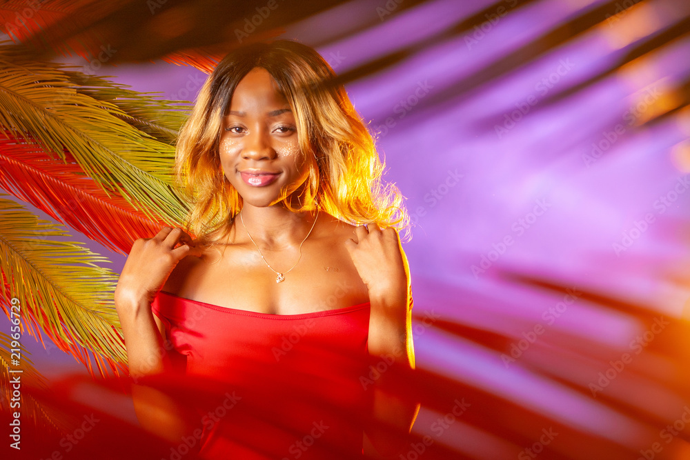 Colored leaves of a palm tree. A girl looks through the leaves of a palm tree. African photo model. A hot evening. Girl on purple background. Colored leaves of a palm tree. A girl looks through the leaves of a palm tree. African photo model. A hot evening. Girl on purple background.