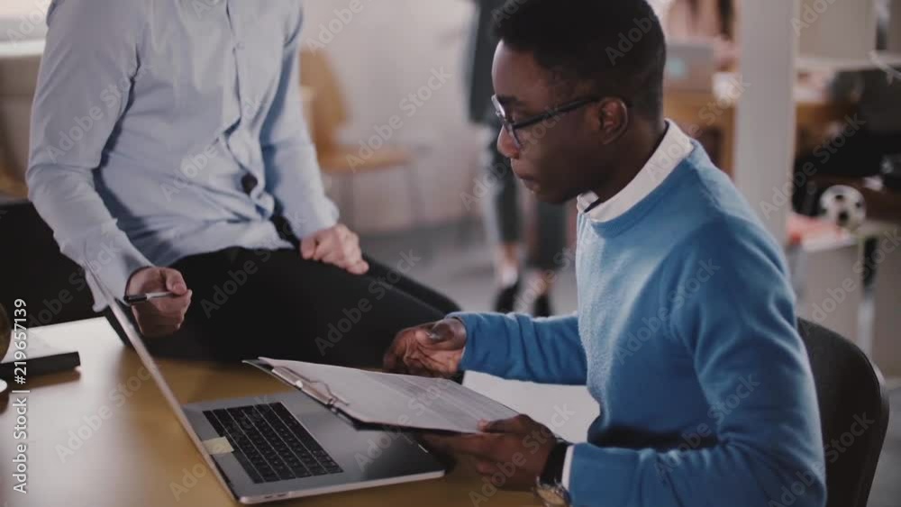 Confident male executive is helping his African American young colleague in modern light coworking, slow motion close-up Confident male executive is helping his African American young colleague in modern light coworking, slow motion close-up