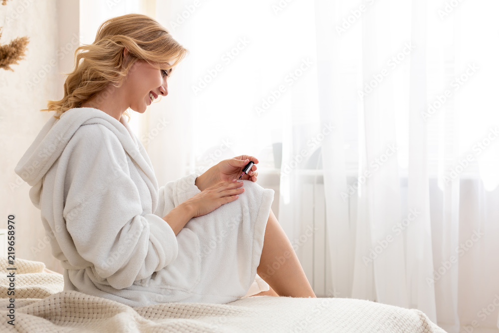 Shapely woman painted her nails in the morning, while sitting on the bed being dressed in a dressing-gown. Shapely woman painted her nails in the morning, while sitting on the bed being dressed in a dressing-gown.