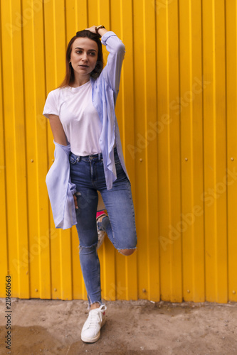 Full length portrait of a happy beautiful woman which wearing white t-shirt, blue shirt and blue jeans looking at camera over yellow background photo