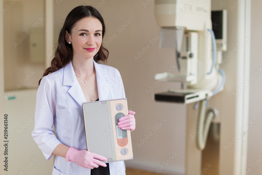 Portrait of the young cheerful breast specialist in pink gloves who is standing near the apparatus of the ultrasound examination of the breast in her office Portrait of the young cheerful breast specialist in pink gloves who is standing near the apparatus of the ultrasound examination of the breast in her office