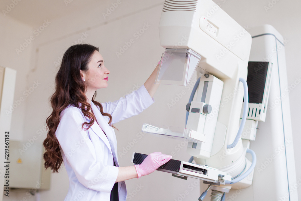 Side view of the young cheerful breast specialist in pink gloves who is preparing the apparatus of the ultrasound examination of the breast for the ultrasound examination in her office Side view of the young cheerful breast specialist in pink gloves who is preparing the apparatus of the ultrasound examination of the breast for the ultrasound examination in her office