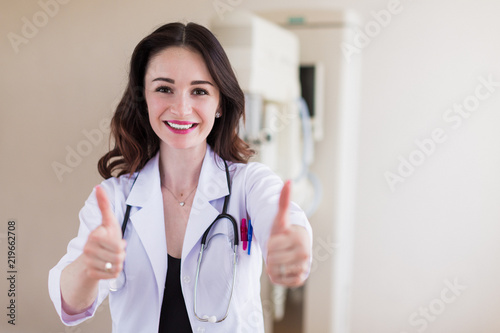 Portrait of the young beautiful breast specialist who is standing in her office and showing thumbs up and smiling