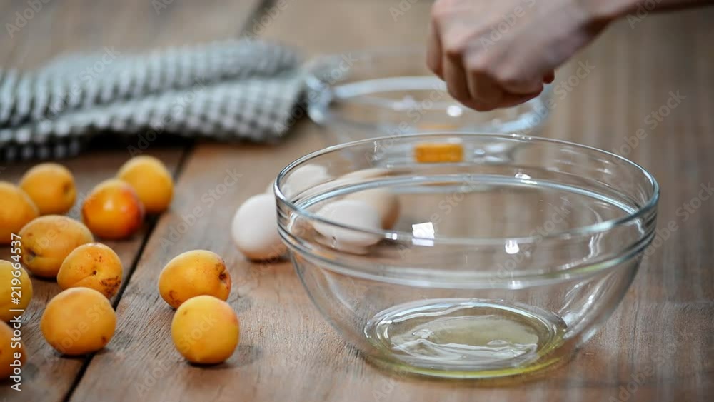 Separating yolk and white of the white shell egg with woman hands above metal stainless steel mixing bowl Separating yolk and white of the white shell egg with woman hands above metal stainless steel mixing bowl