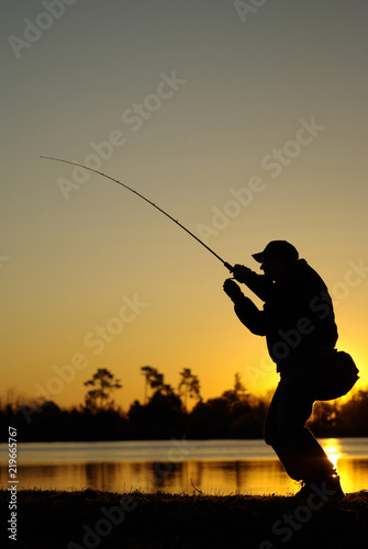 Scène de pêche en eau douce sur un lac. Pêcheur au leurre combattant un poisson au soleil couchant