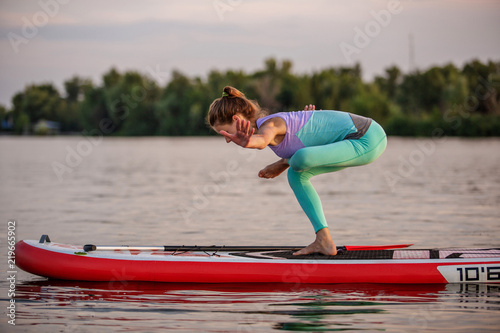 Sporty woman in yoga position on paddleboard, doing yoga on sup board, exercise for flexibility and stretching of muscles