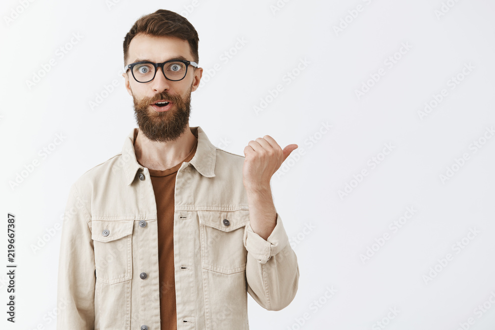 Studio shot of impressed and thrilled charming adult male customer asking question about awesome product in shop staring at camera excited pointing right with thumb holding breath from excitement Studio shot of impressed and thrilled charming adult male customer asking question about awesome product in shop staring at camera excited pointing right with thumb holding breath from excitement