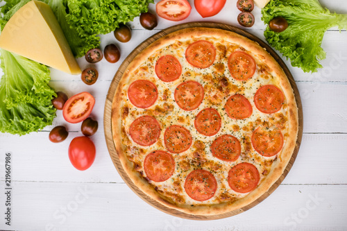 High angle view of fresh pizza on white wooden table surrounded by vegetables and cheese photo