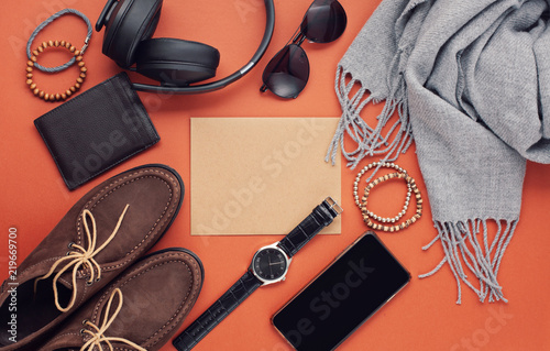 Flat lay of men's accessories with shoes, watch, phone, earphones, sunglasses, scarf over the orange background