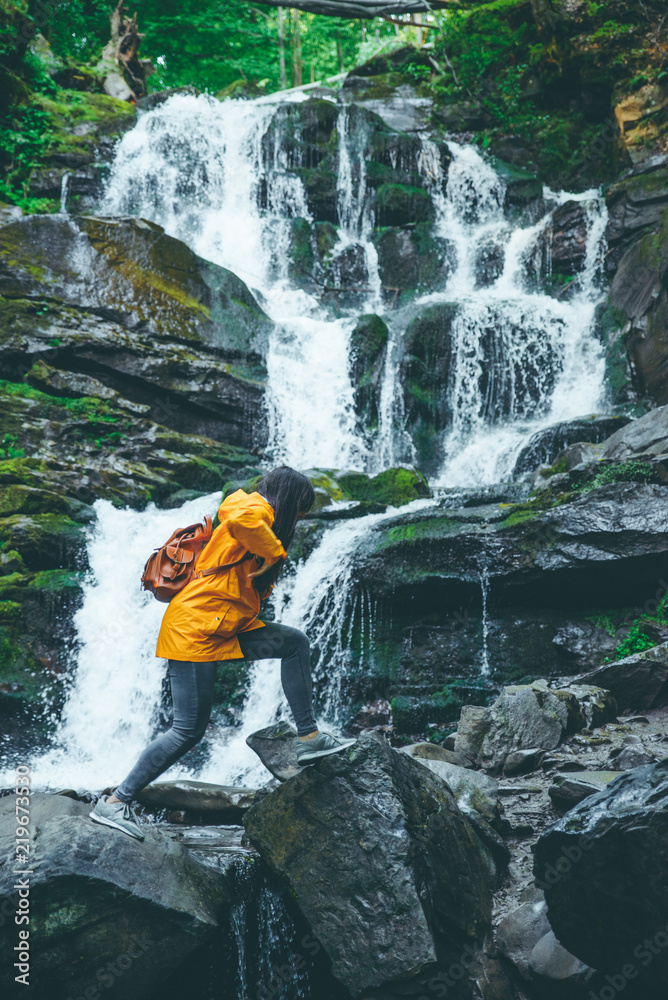 Obraz premium woman jump from rock to rock in forest. water fall on background
