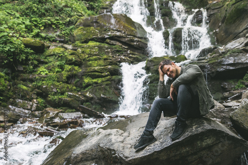 man sitting at rock with waterfall on background