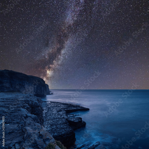 Vibrant Milky Way composite image over landscape of long exposure waves crashing onto rocks