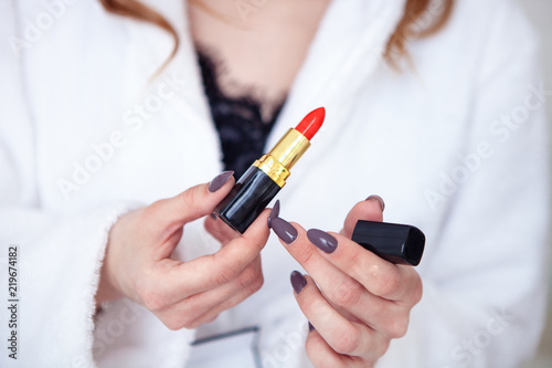 girl is holding a red lipstick on a white lab coat. close-up