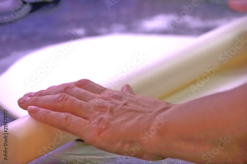 A woman   s hand using a white rolling pin to roll out white sugar paste icing to decorate a cake 