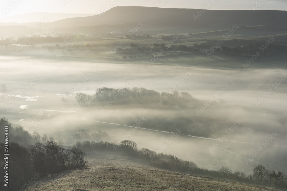 Stunning foggy English rural landscape at sunrise in Winter with layers rolling through the fields