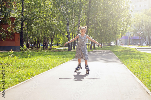 joyful little girl skating on the roller in the city park on a sunny summer day