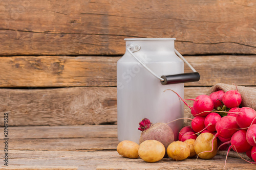 Enamelware milk churn and vegetables. Potatoes, radishes and beetroot on wooden background. photo