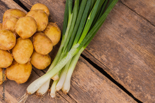 Pile of fresh raw potatoes and green onions. Top view. Old rustic wooden desk background.