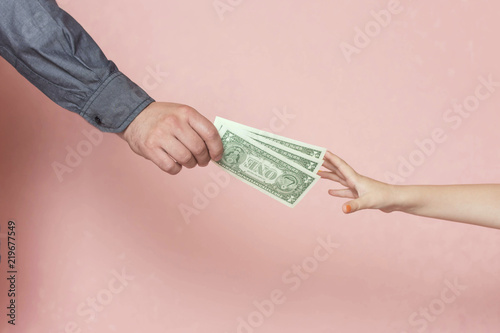 Father gives his daughter pocket money. On the background the child's hand stretches for money.
