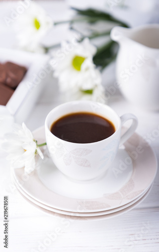 Porcelain cup of black coffee and chrysanthemums flowers on a white background