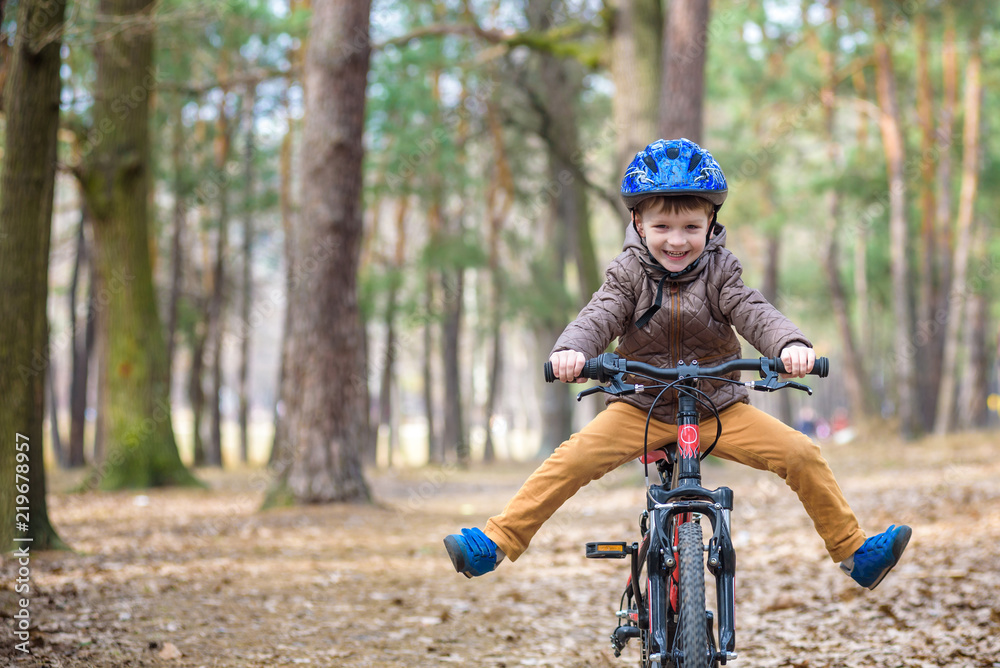 Naklejka premium Happy kid boy of 3 or 5 years having fun in autumn forest with a bicycle on beautiful fall day. Active child wearing bike helmet. Safety, sports, leisure with kids concept.