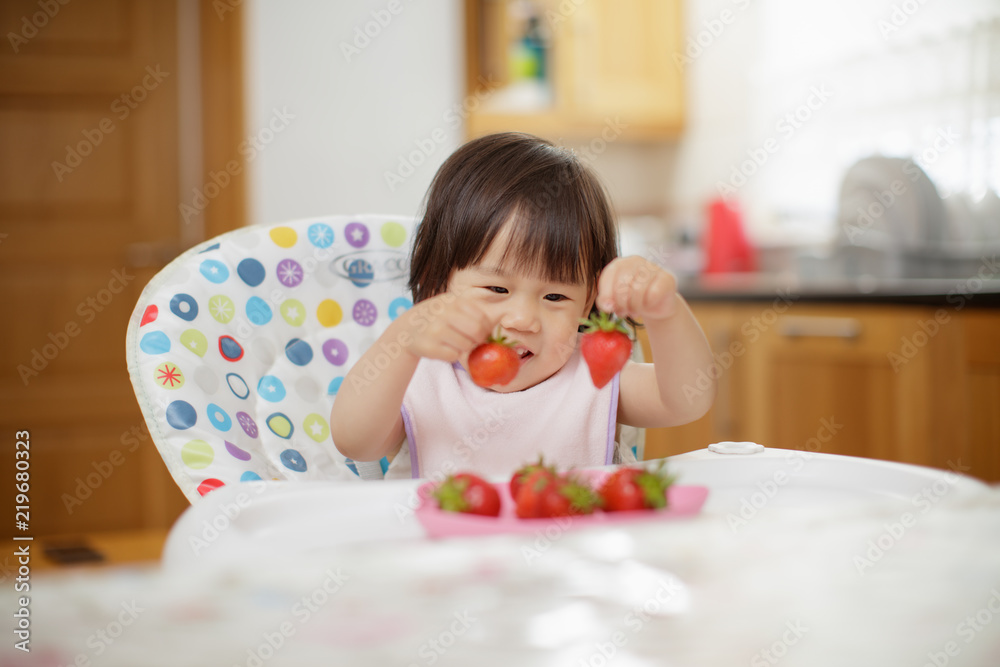 baby girl eating strewberry at home kitchen