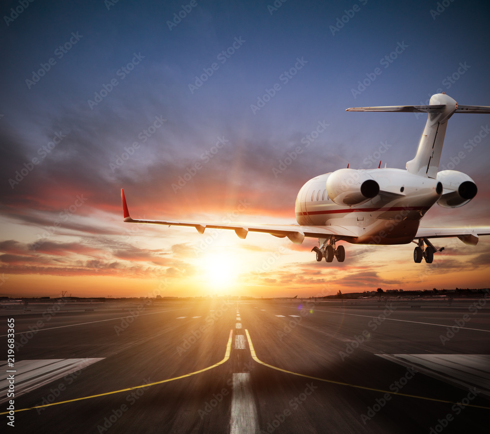 Obraz premium Private jet plane landing on runway in beautiful sunset light.