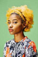 Portrait of a lovely young girl with bleached curly hair looking at camera, in front of a green background