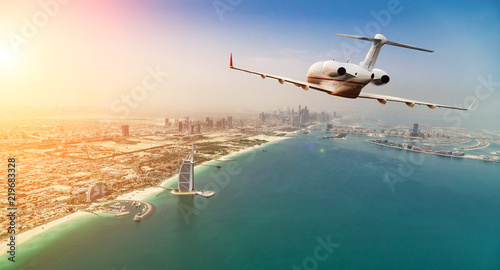 Private jet plane flying above Dubai city in beautiful sunset light.