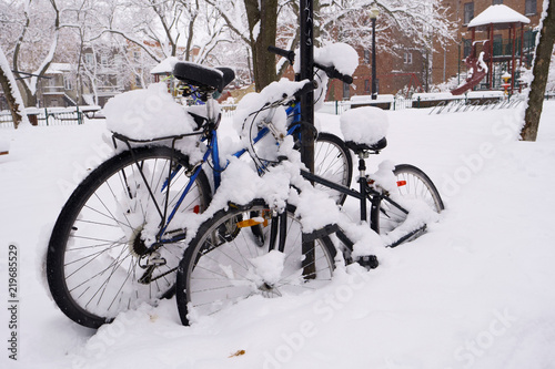 First snow has fallen on everything during the night.  Two bikes are covered of snow in a public park.