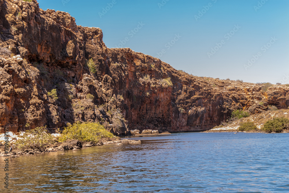 Exmouth, Western Australia - November 27, 2009: Yardie Creek Gorge in Cape Range National Park on North West Cape. Wide shot of Red rock cliffs between blue water and sky. Some green vegetation.