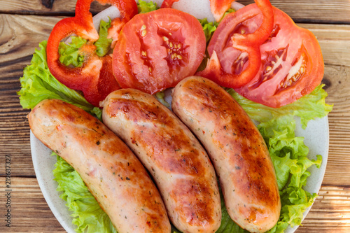 Grilled sausages with fresh vegetables on wooden table