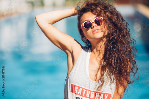 Young sensual pretty woman posing on the beach , stylish modern hipster outfit, luxury vacation mood.hot summer fashion accessory,stylish sunglasses.Sexy perfect fit body woman