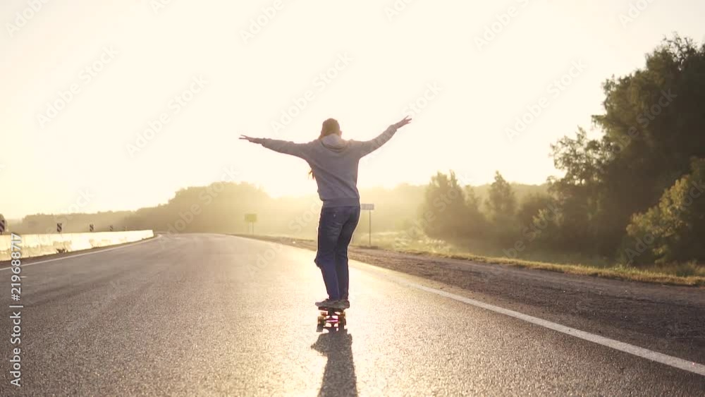 young red-haired girl on a skateboard on a deserted highway at sunset. The girl enjoys freedom and loneliness. Back view. slow motion young red-haired girl on a skateboard on a deserted highway at sunset. The girl enjoys freedom and loneliness. Back view. slow motion
