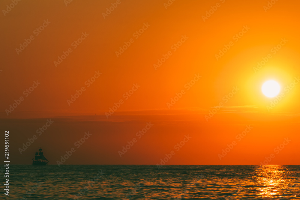 a sea landscape with a setting sun and a sailboat