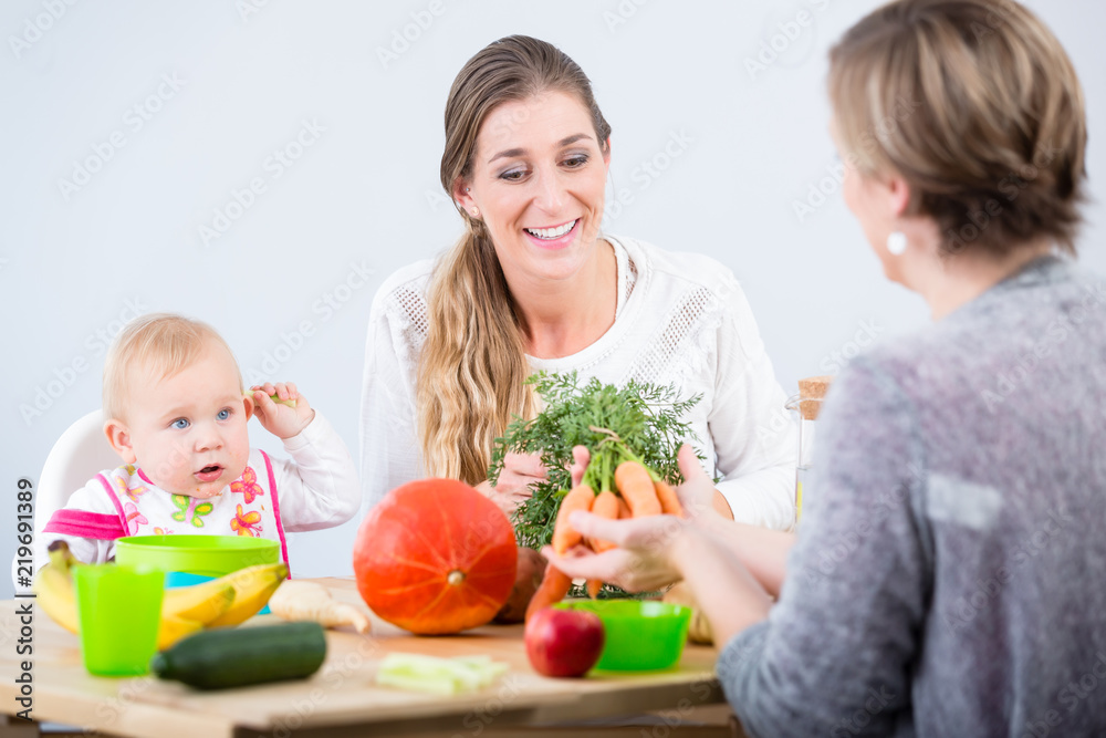 Portrait of a cheerful woman and young mother of a cute baby girl, learning from her best friend how to prepare healthy solid food from natural ingredients