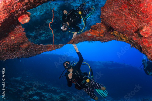 A SCUBA diver with a perfect reflection from trapped air bubbles on an underwater rocky overhang on a coral reef