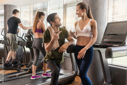 Cheerful young man and woman chatting while having break from running exercise in modern gym 