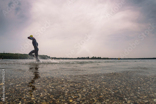 A triathlete in a wetsuit runs out of the water