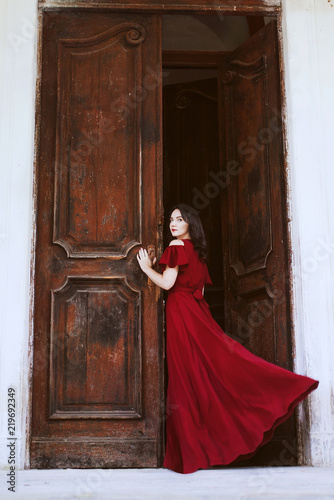 Beautiful woman in a red dress standing near a big wooden door.