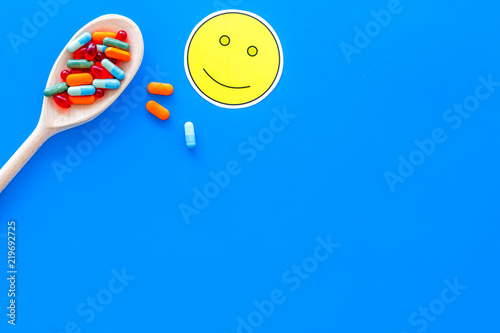 Reception of medicines concept. Recovery. Pills in spoon near smile face emoji on blue background top view space for text