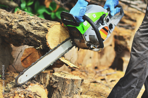 A man in blue mitts cuts a piece of wood from a chainsaw photo